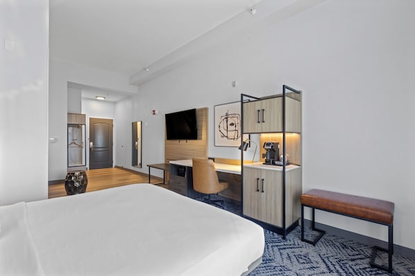 A modern hotel room with a large bed, a desk, a chair, a wardrobe, and a television.