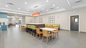 A modern dining area with wooden tables and chairs, a central island, and framed artwork on the walls. - Country Inn & Suites by Radisson, Savannah Airport, GA (Savannah)