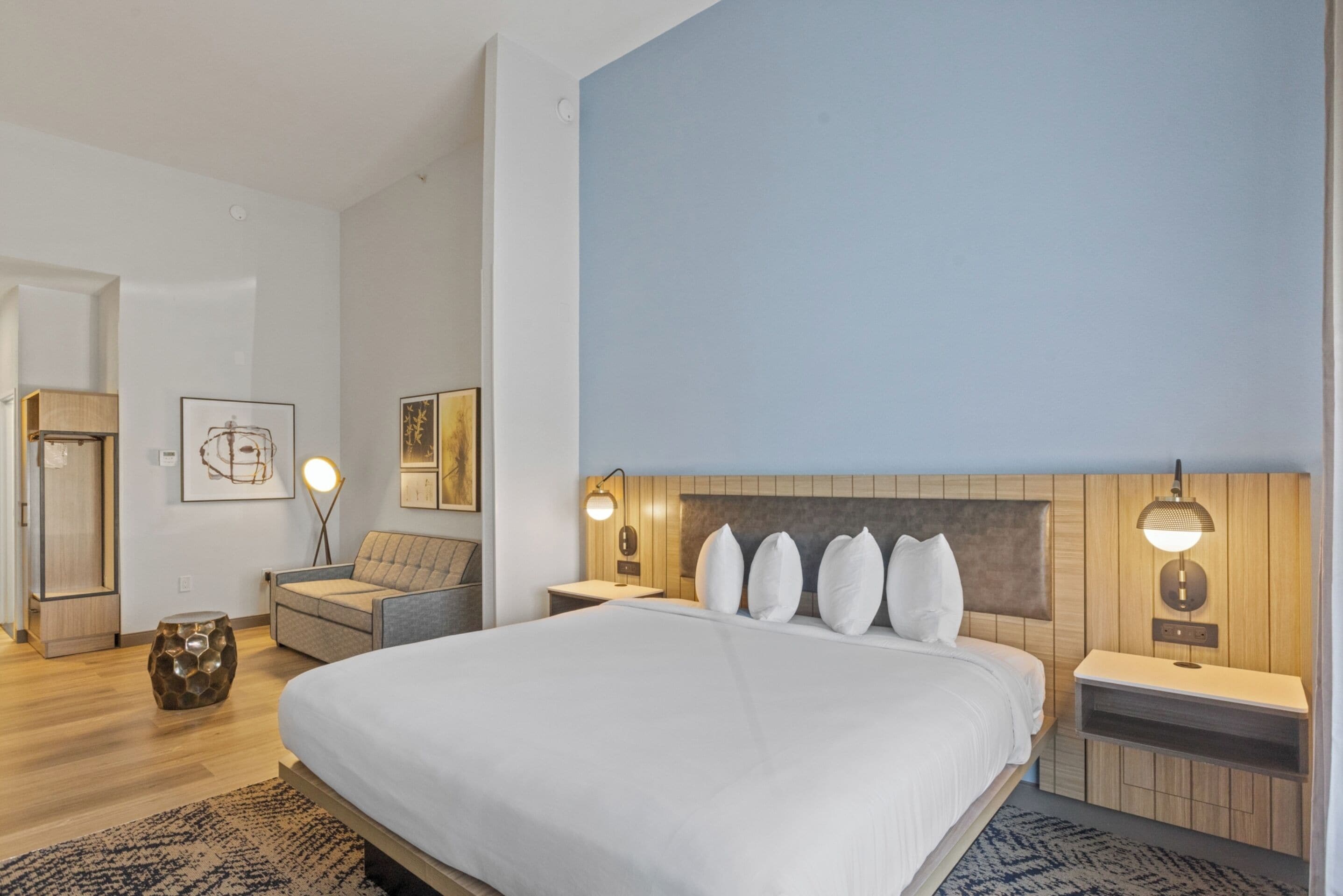 Een moderne hotelkamer met een groot bed, een houten hoofdbord, nachtkastjes met lampen, een bank en een klein decoratietafeltje.