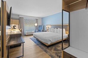 A modern hotel room with a large bed, a desk, a flat-screen TV, and a seating area with a view of the outdoors.