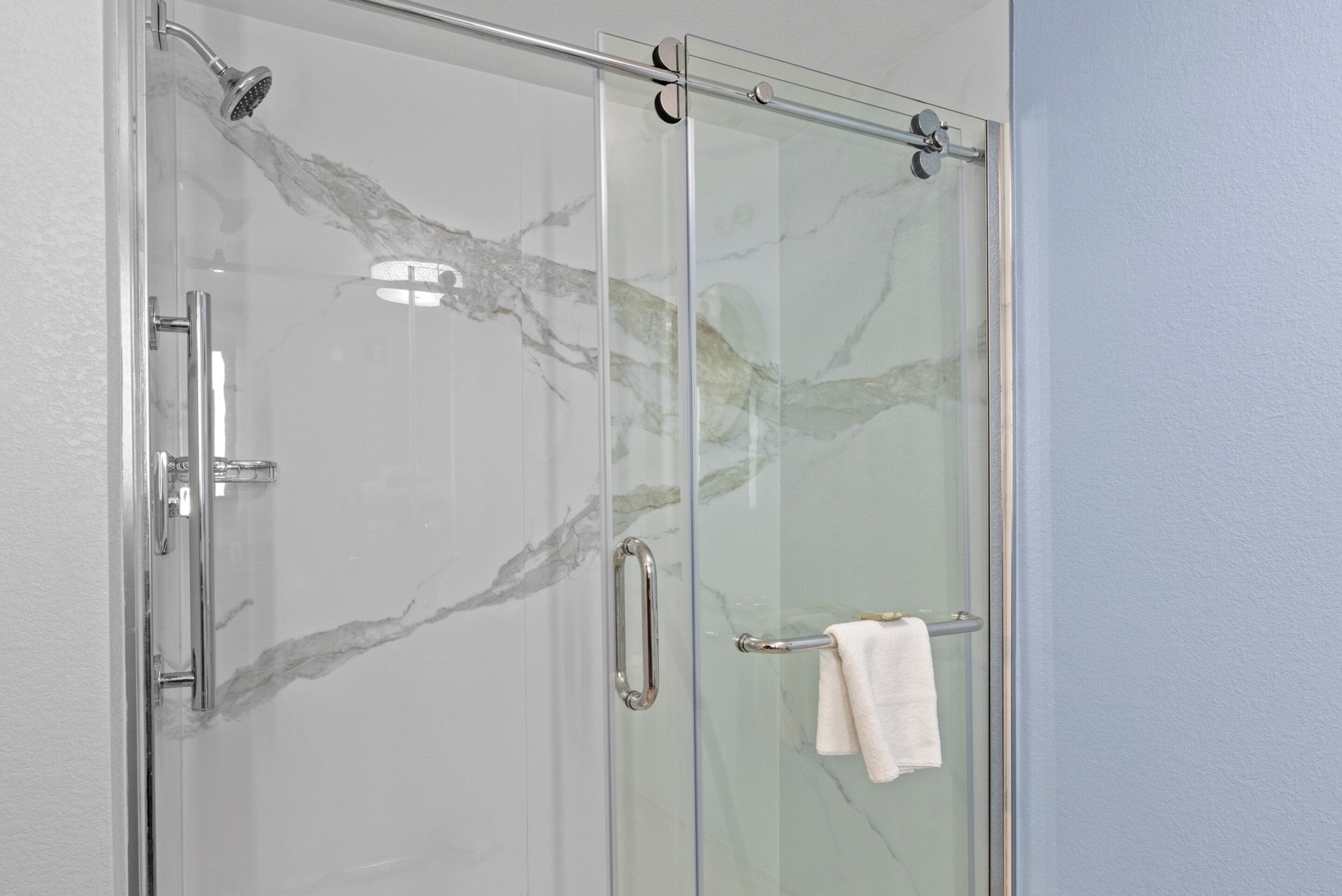 A glass-enclosed shower with a marble design, a towel rack, and a glass door.