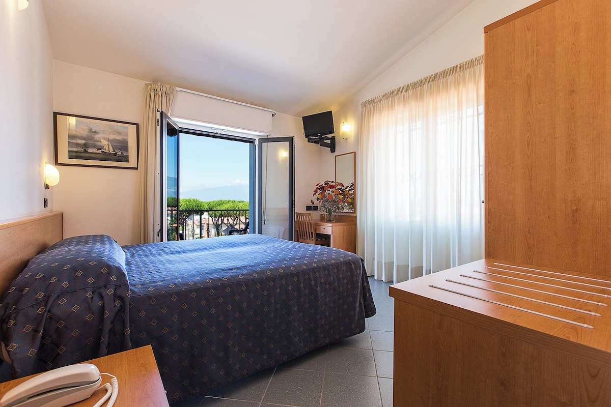 Une chambre d’hôtel équipée d’un lit, d’un bureau, d’une chaise, d’un téléphone et offrant une vue sur l’extérieur.