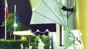Eine Statue einer Frau, ein Springbrunnen und ein Tisch mit Stühlen vor einem Gebäude bei Nacht.