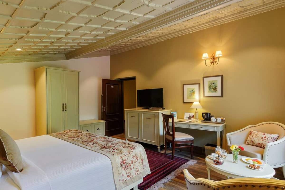 Habitación de hotel con cama, escritorio con computadora, televisión y zona de comedor con mesa y sillas.