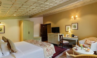 Quarto de hotel com uma cama, uma mesa de escritório com computador, televisão e área de refeições com mesa e cadeiras.