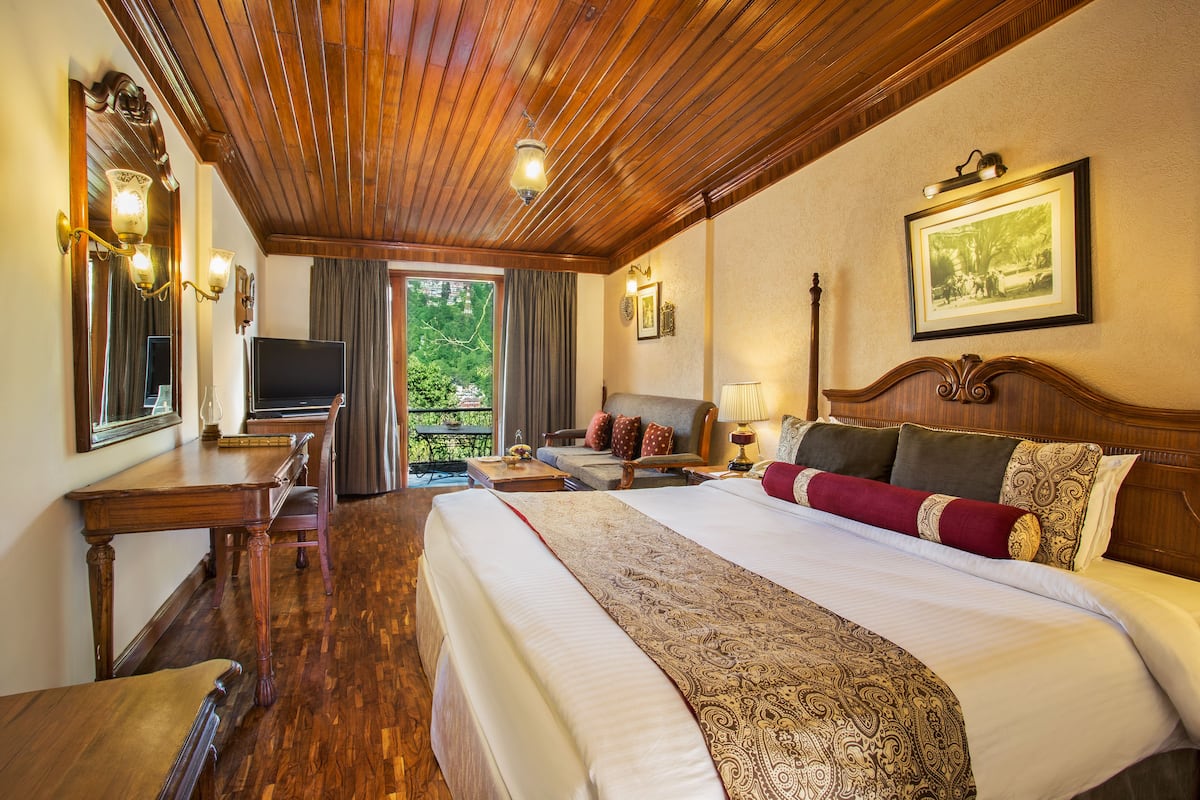 Habitación de hotel con una cama grande, techo de madera, televisión, escritorio y vistas a zonas verdes.
