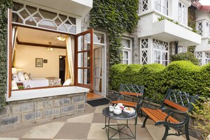Habitación de hotel con un ventanal grande, una cama, una mesita de noche con lámpara y vistas al jardín.