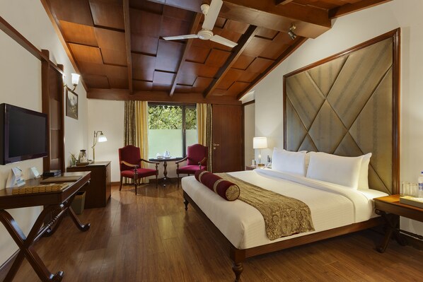 A hotel room with a large bed, wooden ceiling, a television, a desk, and a chair.