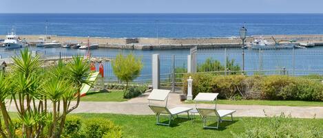 Vista costera con un puerto deportivo, mesas al aire libre y cielo despejado.