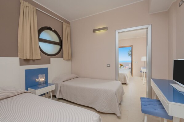 A hotel room with two beds, a desk, a TV, and a view of the beach.