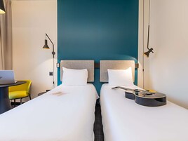 Habitación de hotel con dos camas, un escritorio, una laptop, una guitarra y una silla amarilla.