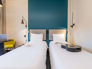 A hotel room with two beds, a desk with a laptop, a guitar, and a yellow chair.