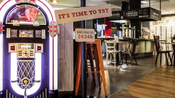 Um jukebox com letreiro de neon, um letreiro de boas-vindas, uma placa indicando a hora de experimentar e um letreiro de bar/lanches.