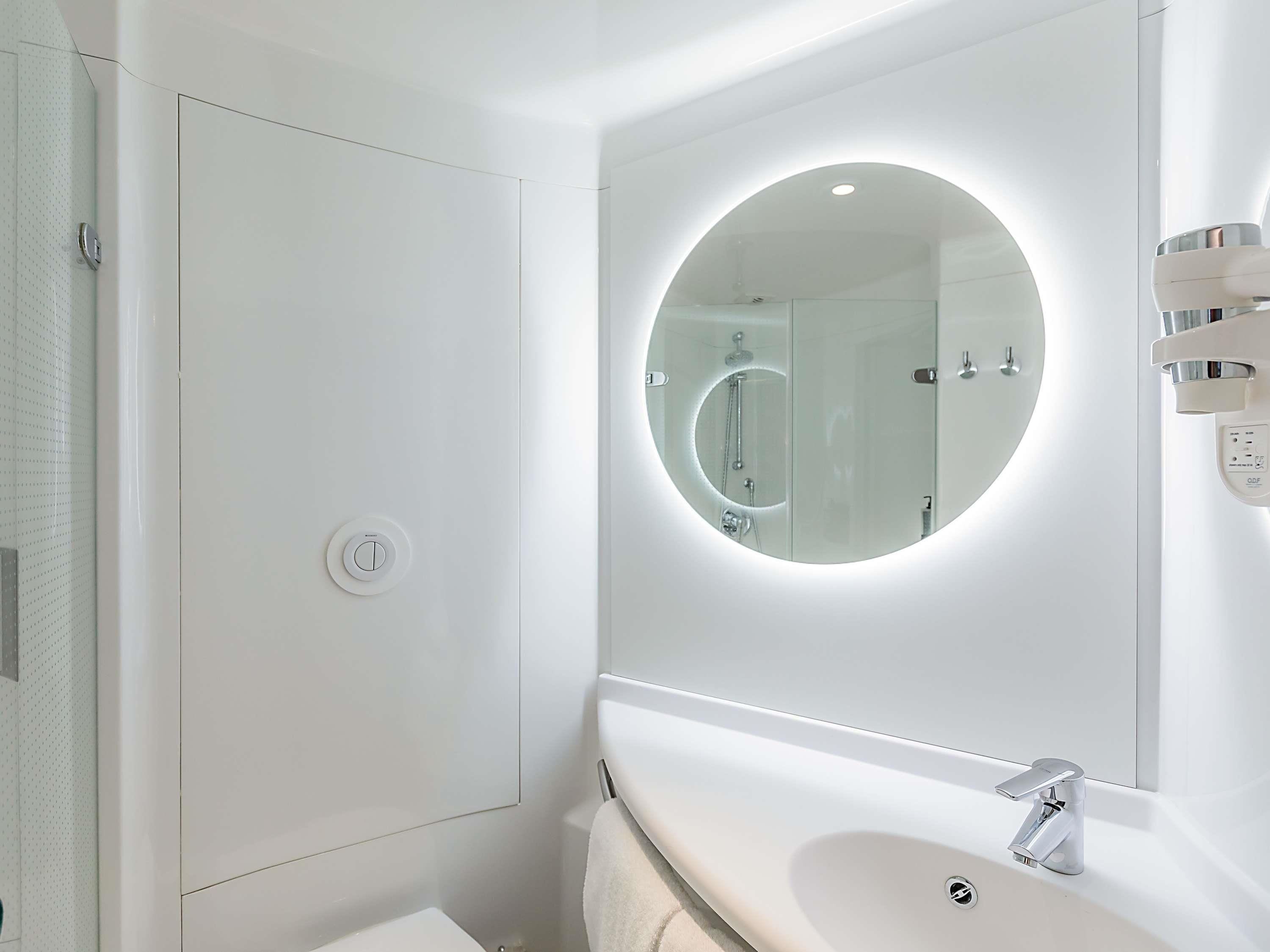 Un baño moderno con un espejo redondo, un lavabo blanco y una cabina de ducha de vidrio.
