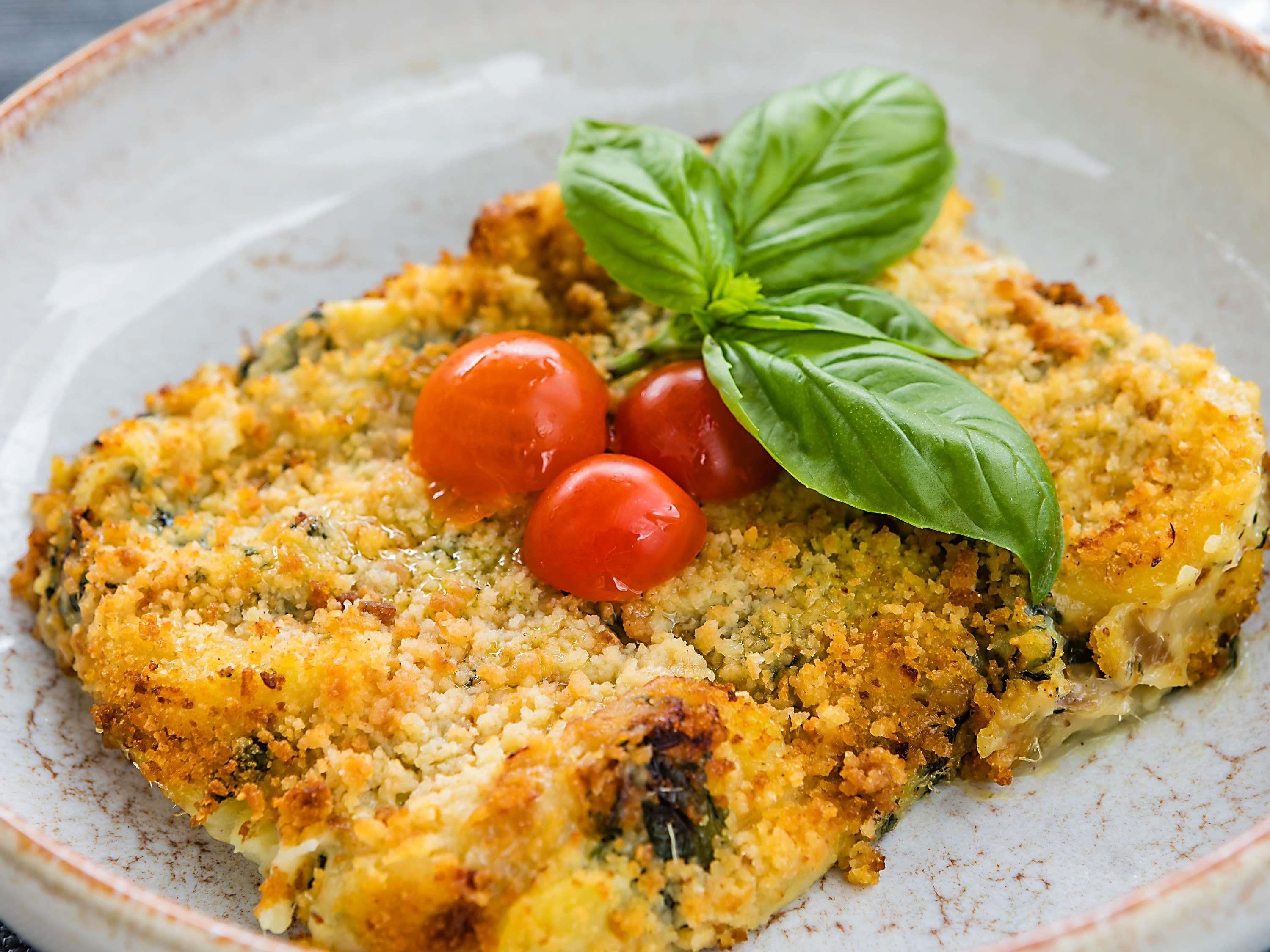 A dish with a golden-brown crust, cherry tomatoes, and a basil leaf on a ceramic plate.
