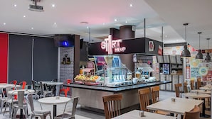 Zona de comida con un letrero de neón, zonas de estar y un mostrador con productos alimenticios.