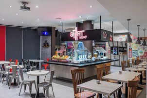 Zona de comida con un letrero de neón, zonas de estar y un mostrador con productos alimenticios.