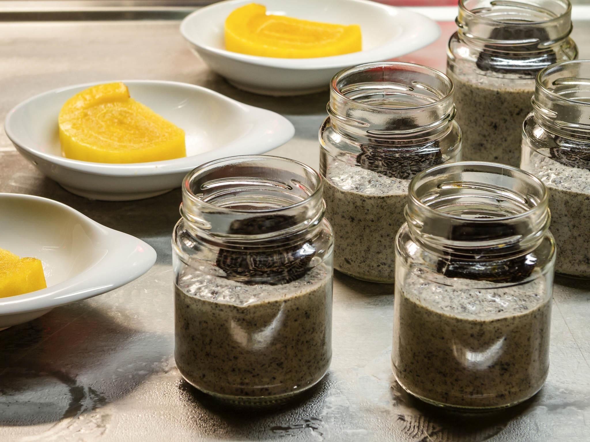 A kitchen counter with several glass jars containing a dark mixture, possibly a smoothie or sauce, and a few white plates with yellow slices of fruit.