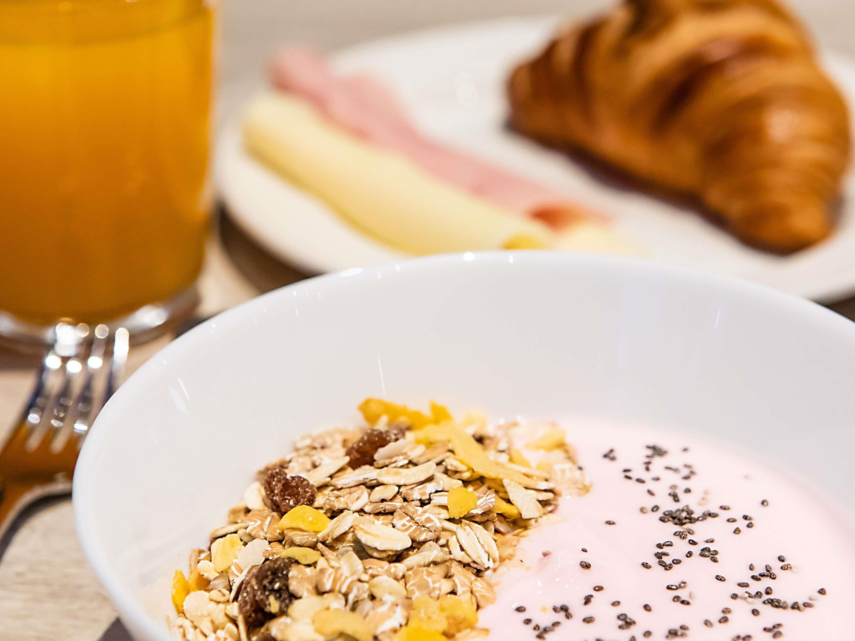 Une table mise pour le petit-déjeuner avec un bol de céréales, un croissant et un verre de jus d’orange.