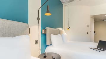 Ein modernes Hotelzimmer mit einem großen Bett, einem Schreibtisch mit einem Laptop, einem Nachttisch mit einer Fernbedienung und zwei Pendelleuchten.