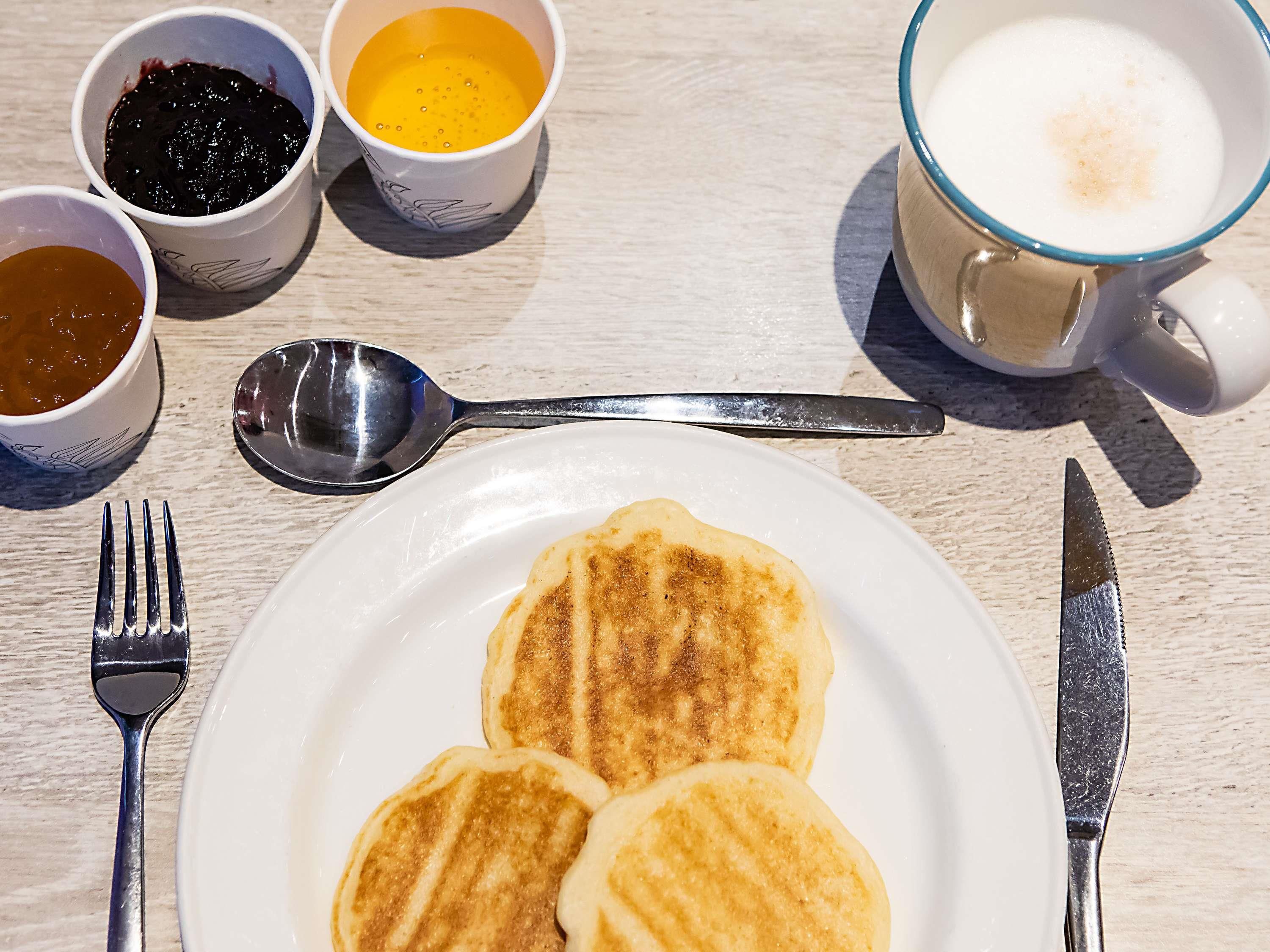 Desayuno con tortitas, café y mermelada sobre una mesa de madera.