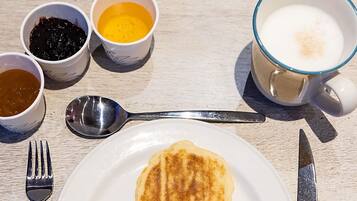 Desayuno con tortitas, café y mermelada sobre una mesa de madera.