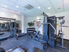 Un gimnasio con diferentes equipos de ejercicio, un cartel en la pared que dice 'Good Vibe Only' y un espejo que refleja los equipos.
