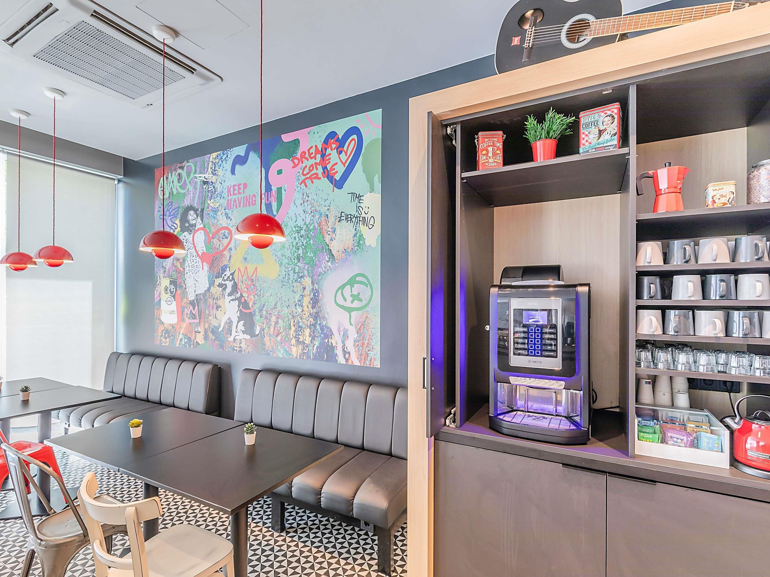 A modern room with a large wall mural, a coffee machine, and a seating area with a table and chairs.