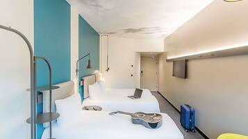 Quarto de hotel moderno com uma cama, um violão, um laptop e uma TV na parede.