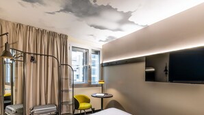 A hotel room with a bed, a chair, a small table, a TV, and a window with curtains. - ibis Lisboa Alfragide (Amadora)
