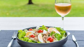Een saladekom met sla, kerstomaatjes, tonijn en gekookte eieren, vergezeld van een glas wijn op een tafel.