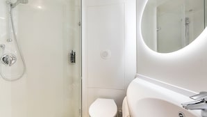 Un baño moderno con ducha de vidrio, inodoro y lavamanos con espejo.