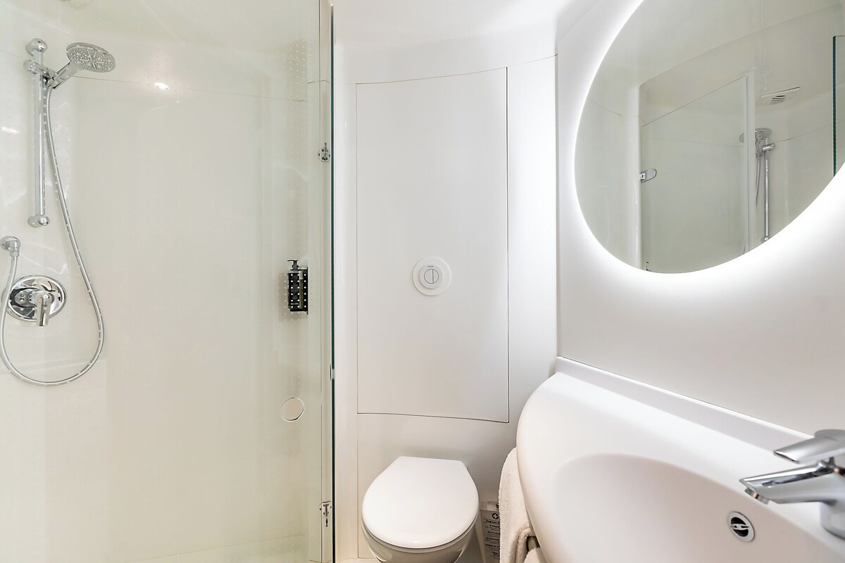 Un baño moderno con ducha de vidrio, inodoro y lavamanos con espejo.