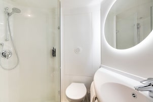 Un baño moderno con ducha de vidrio, inodoro y lavamanos con espejo.