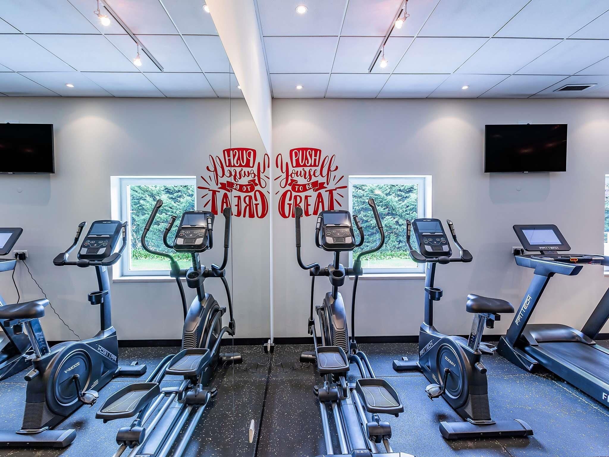 A gym with multiple exercise machines, motivational wall art, and a window with a view of greenery.