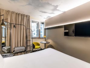 A hotel room with a bed, a chair, a small table, a TV, and a window with curtains. - ibis Lisboa Alfragide (Amadora)