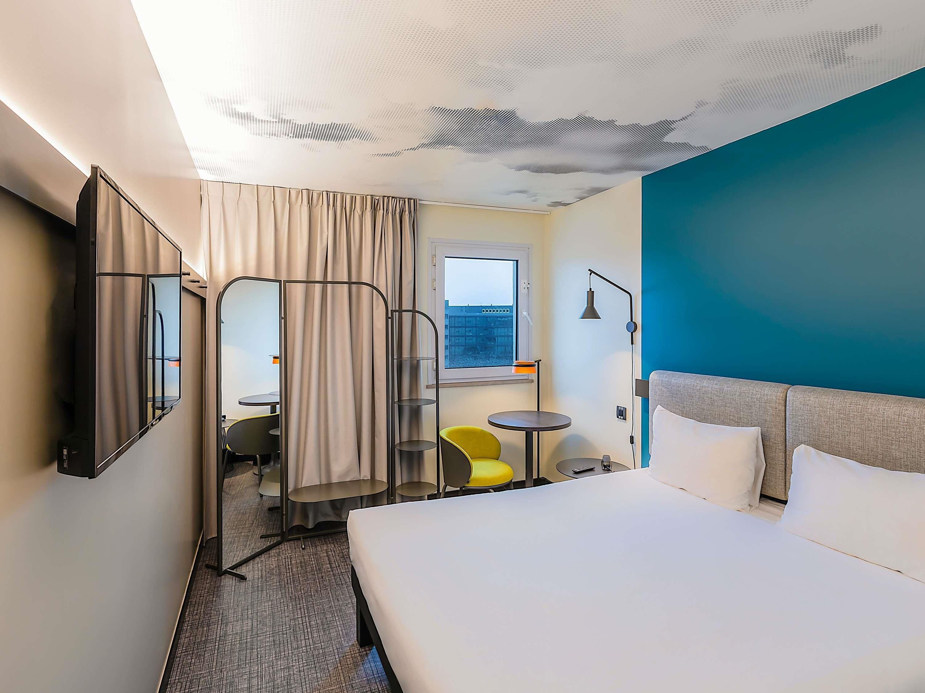 Habitación de hotel con cama, escritorio, silla, mesita, lámpara y ventana con vistas.