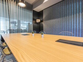 Un salón de conferencias con una mesa de madera, plantas en macetas y una regla negra.