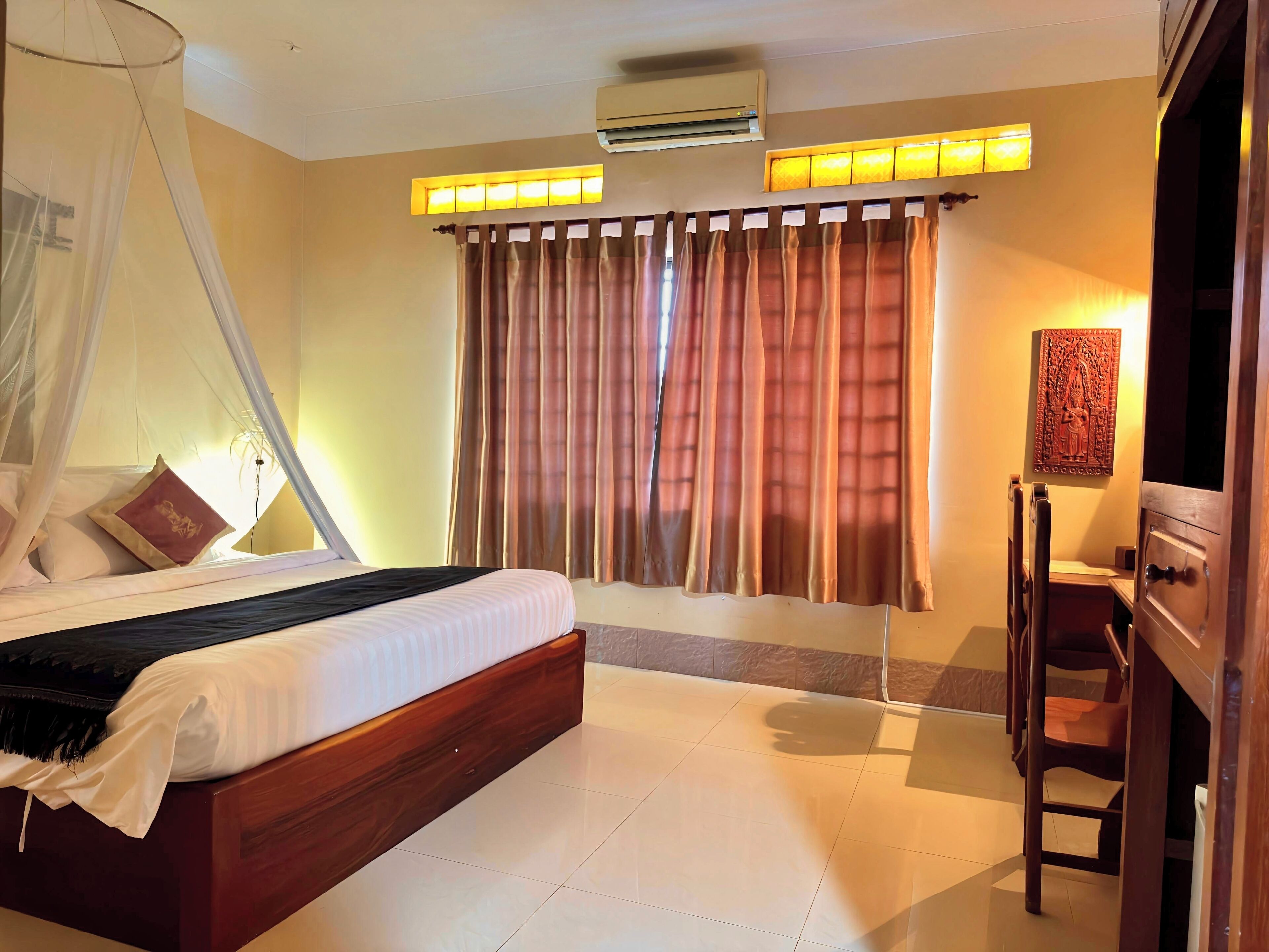 Una habitación de hotel con cama, cortinas, unidad de aire acondicionado y una lámpara fijada a la pared.