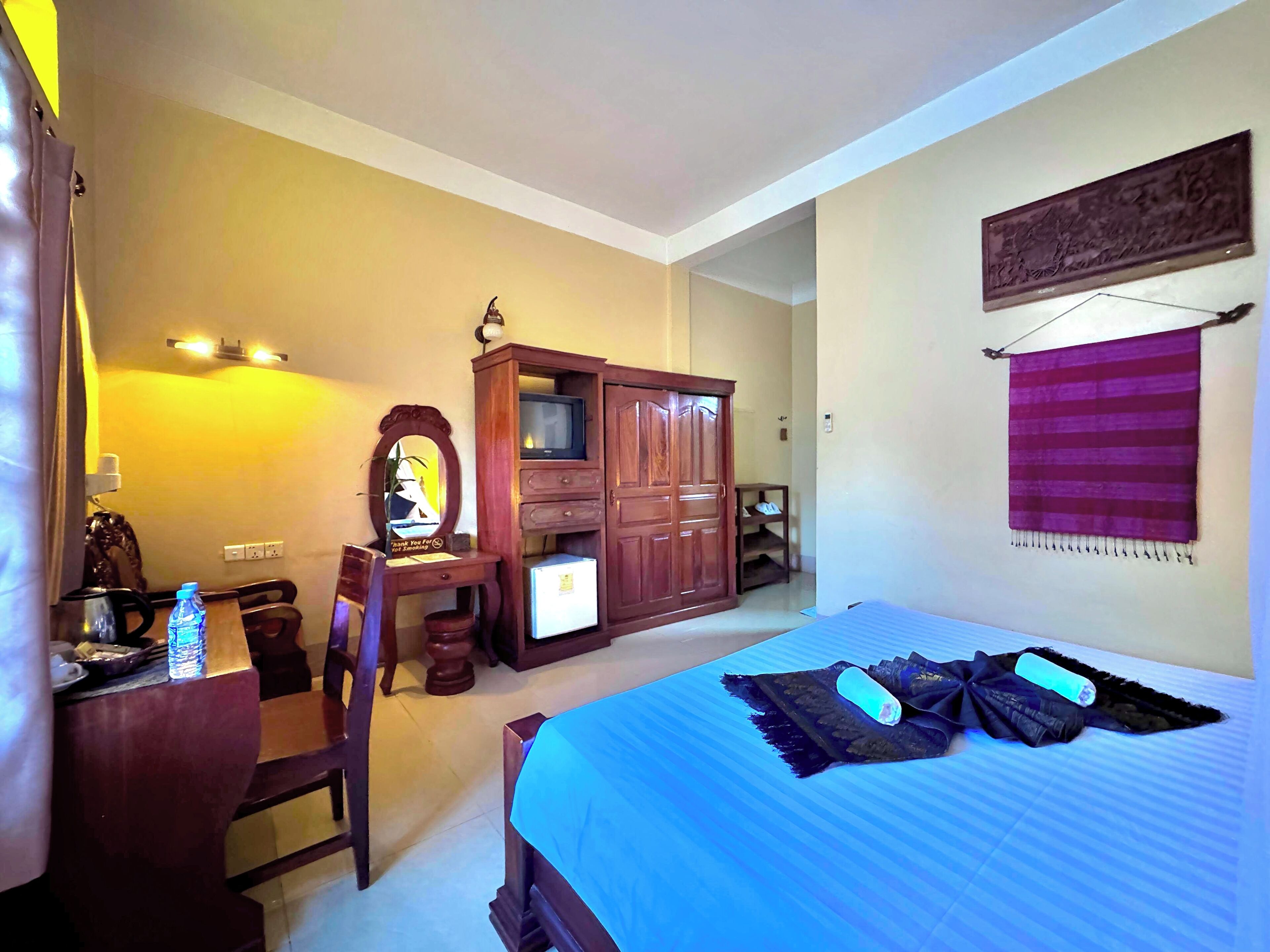 A hotel room with a bed, a desk with a chair, a wardrobe, and a television.