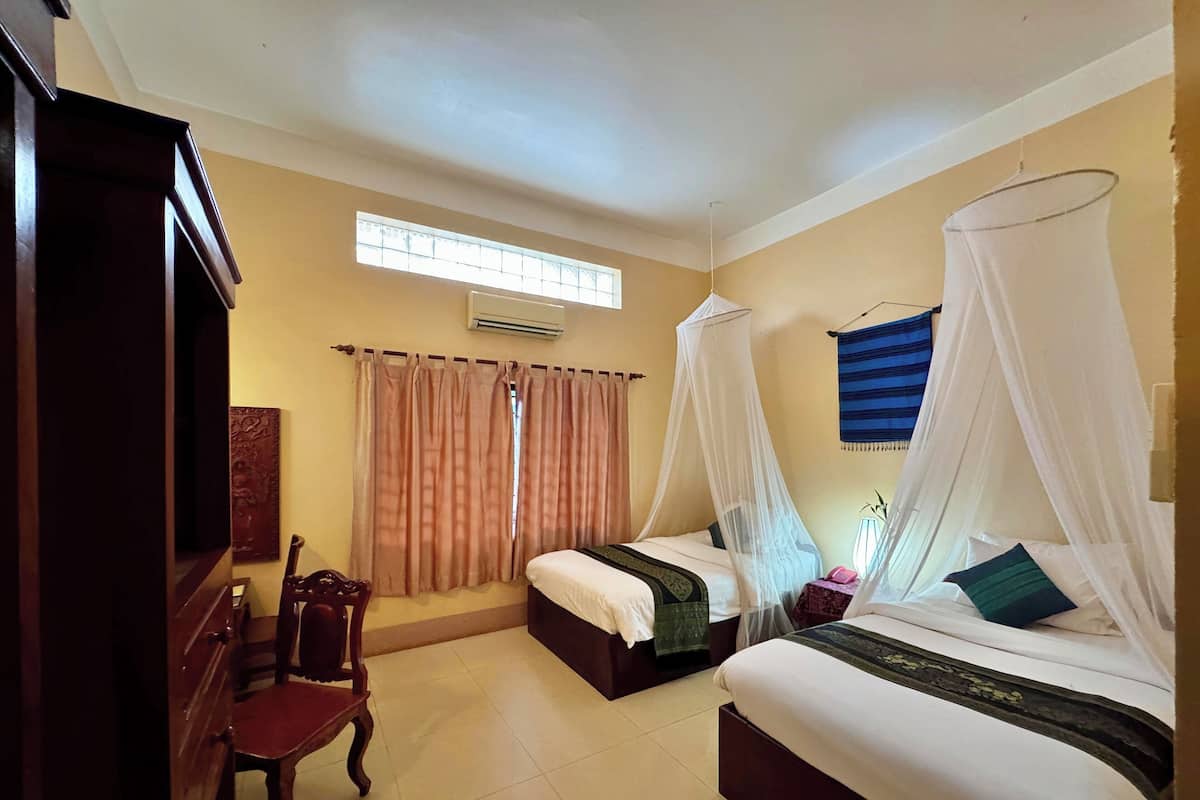 A hotel room with two beds, each with a canopy, a desk with a chair, and a window with curtains.
