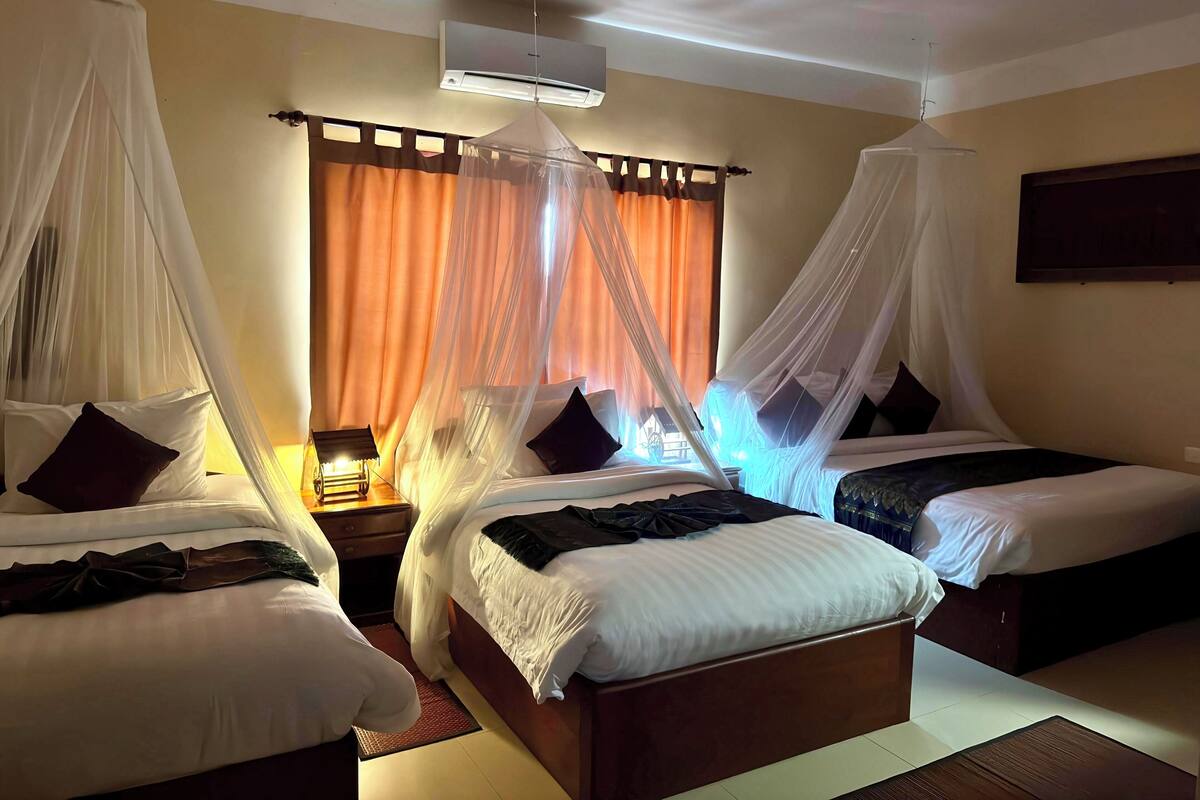 A hotel room with two beds, each with a canopy, a bedside table, and an air conditioning unit on the wall.