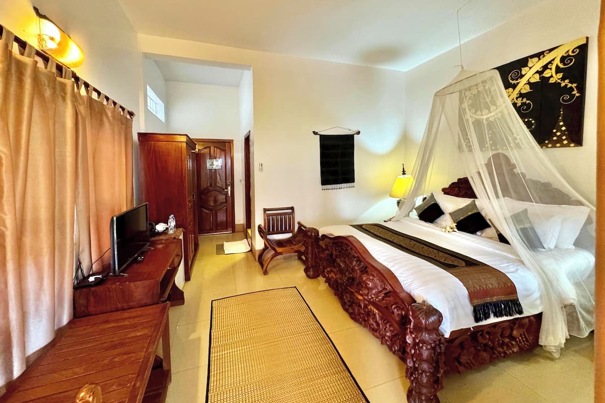 A bedroom with a large bed, a TV, a wooden desk, and a chair.