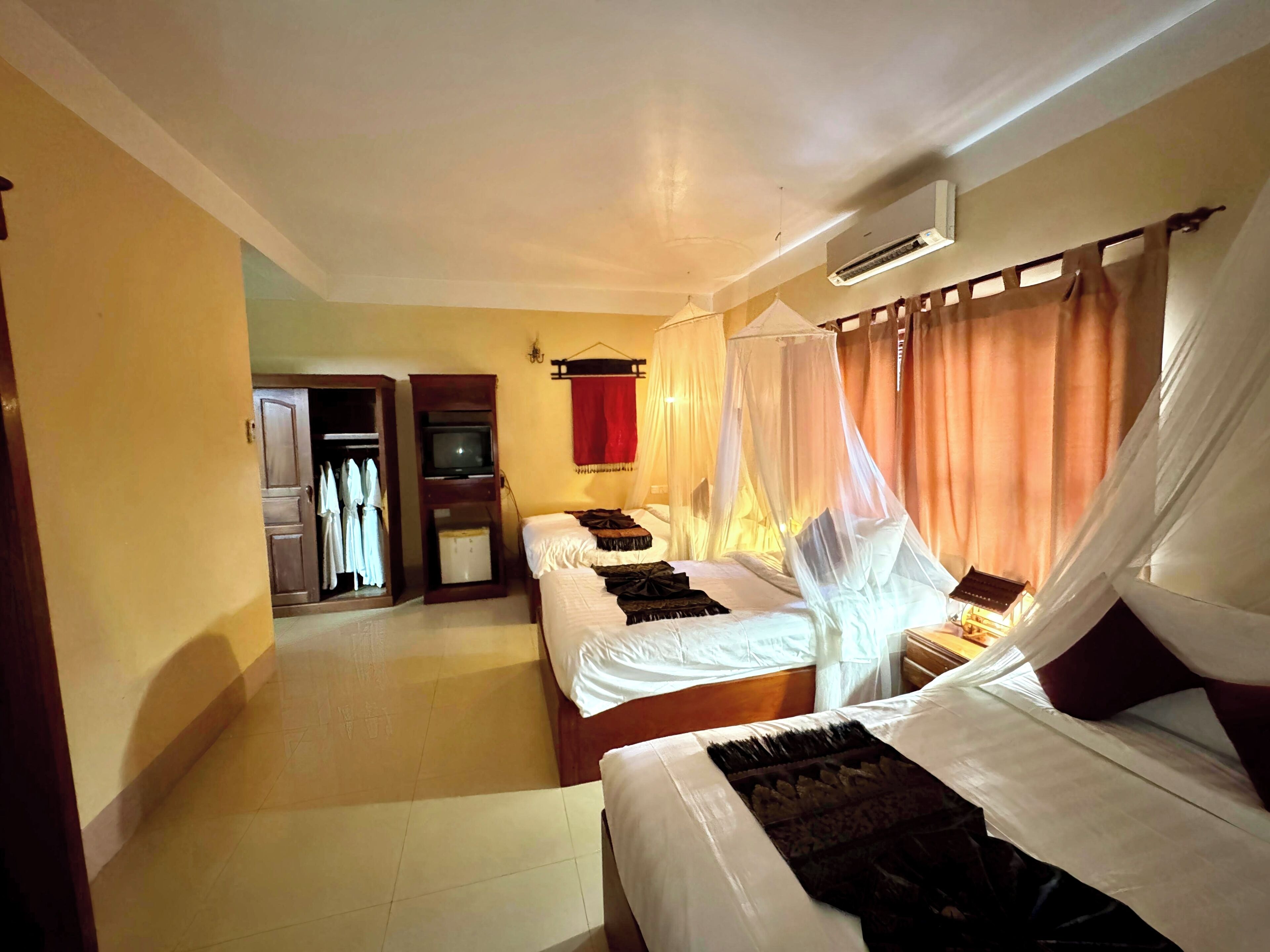 A hotel room with two single beds, a TV, a wardrobe, and a mosquito net.