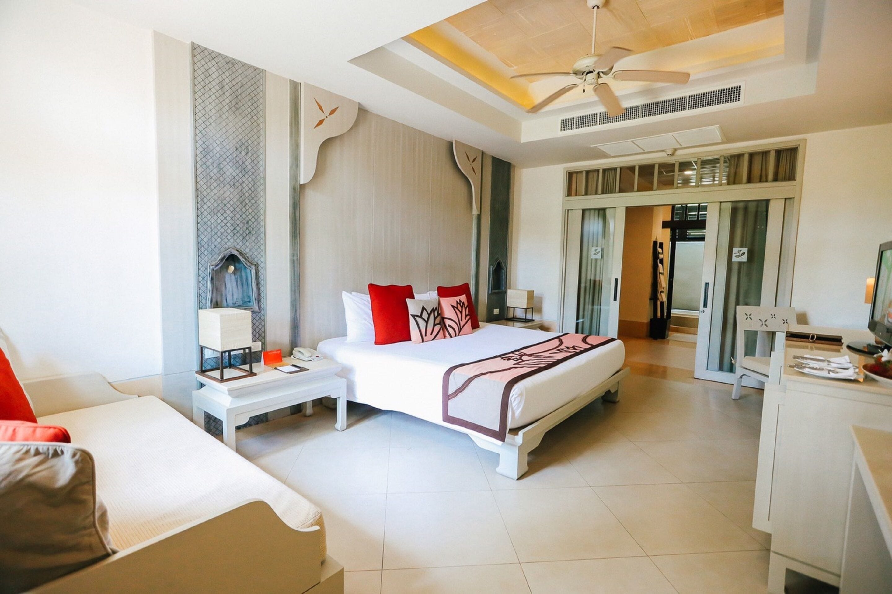 A hotel room with a bed, bedside table, chair, desk, and a ceiling fan.