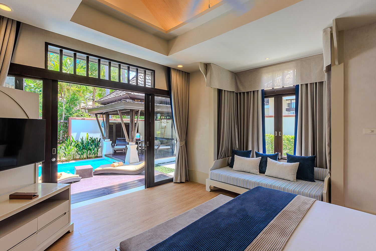 A modern hotel room with a large bed, a television, a desk, and a view of a swimming pool.