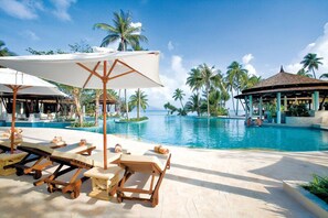 A resort pool area with sun loungers and umbrellas, surrounded by palm trees and a clear sky. - Melati Beach Resort & Spa (Koh Samui)