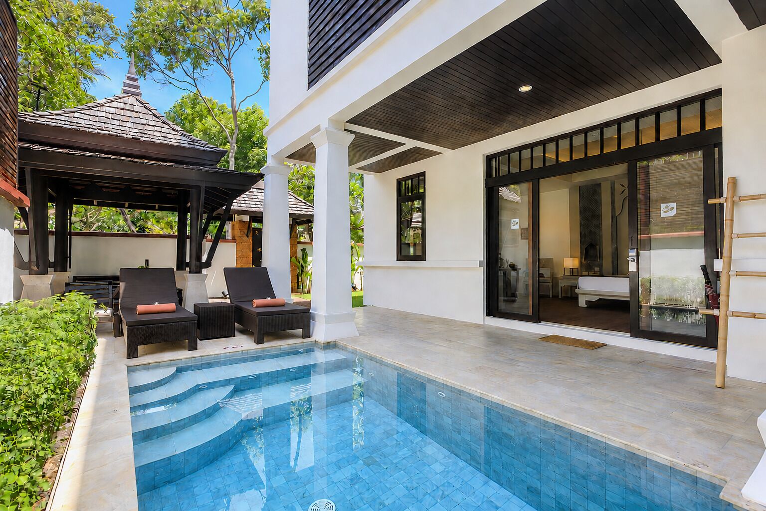 A swimming pool with lounge chairs, a covered seating area, and a modern building with large windows.