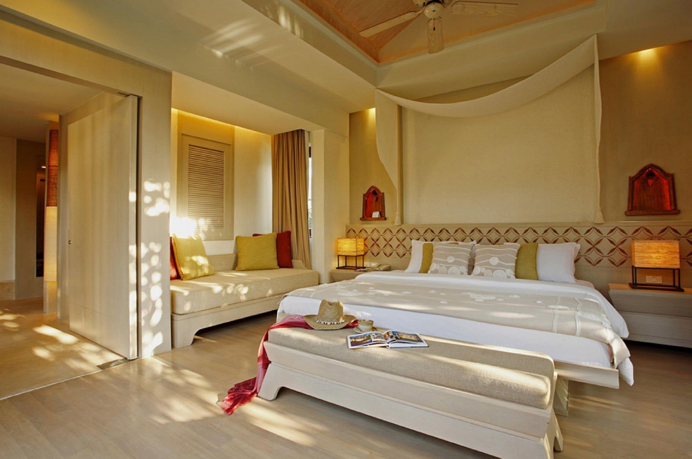 Une chambre d’hôtel avec un grand lit, deux tables de chevet avec des lampes, un canapé et un ventilateur de plafond.