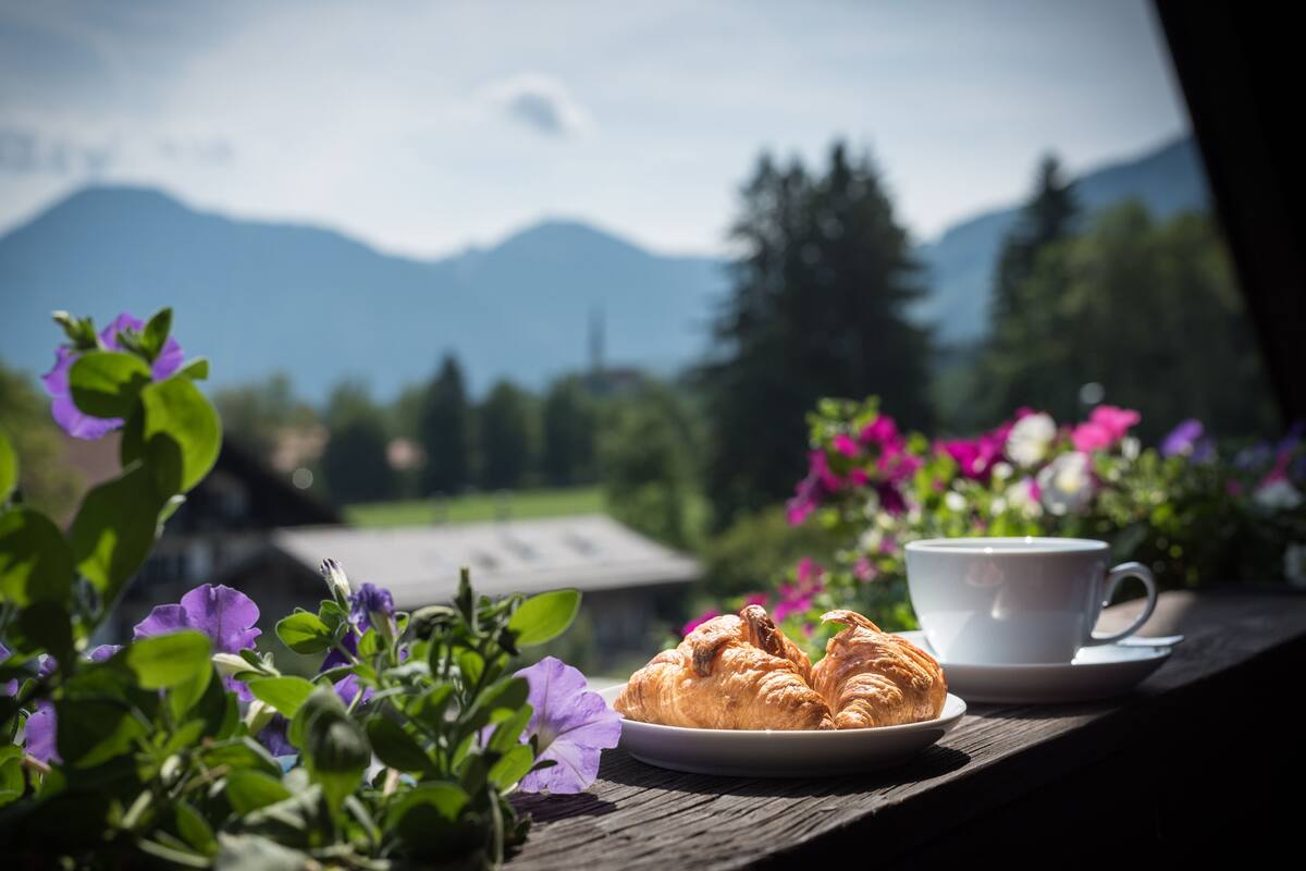 A croissant and a cup on a wooden table with a mountain view in the background.